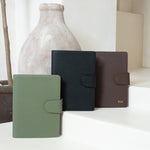Three textured vegan leather folio planner covers in sage green, black, and dark brown