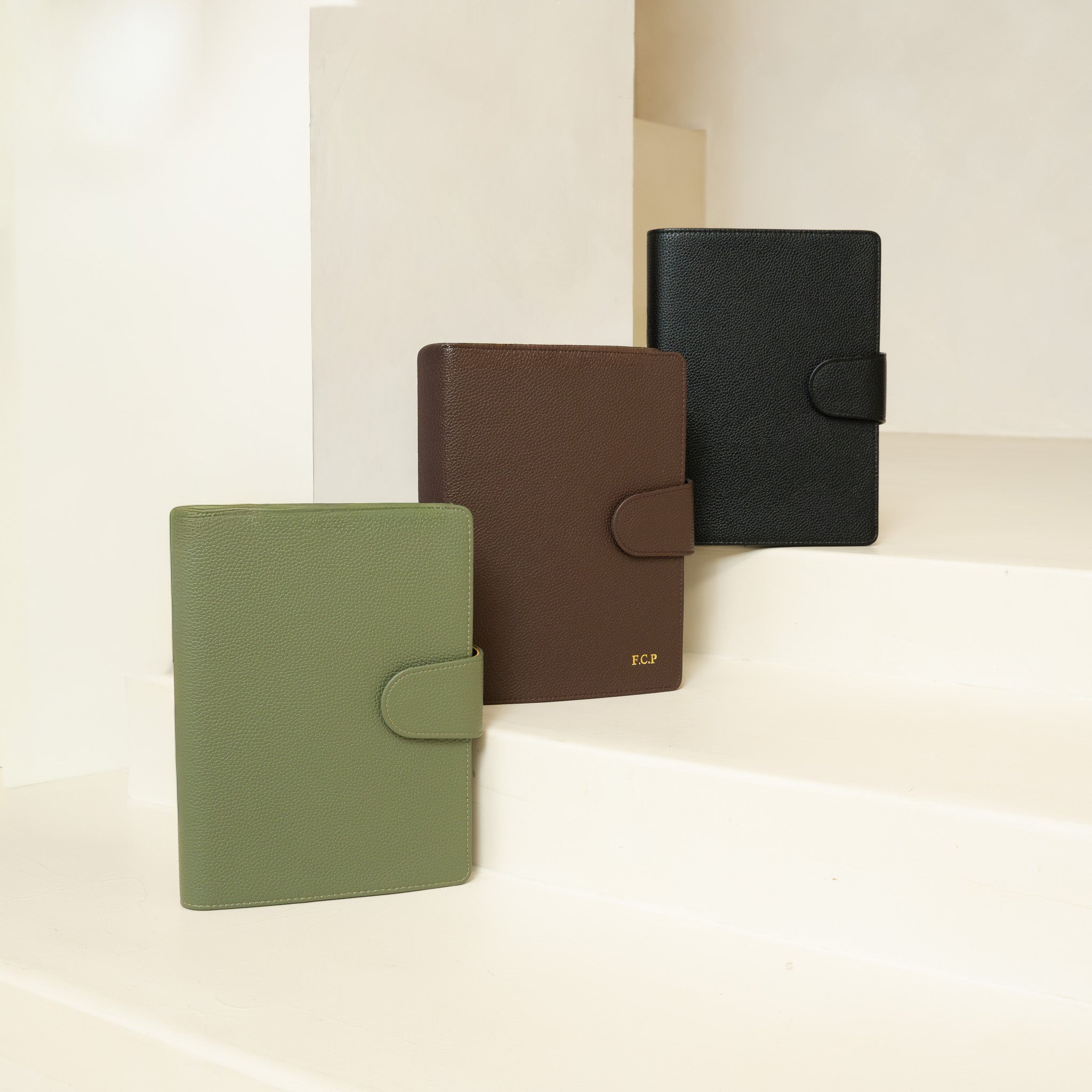 Three textured vegan leather folio planner covers in sage green, black, and dark brown
