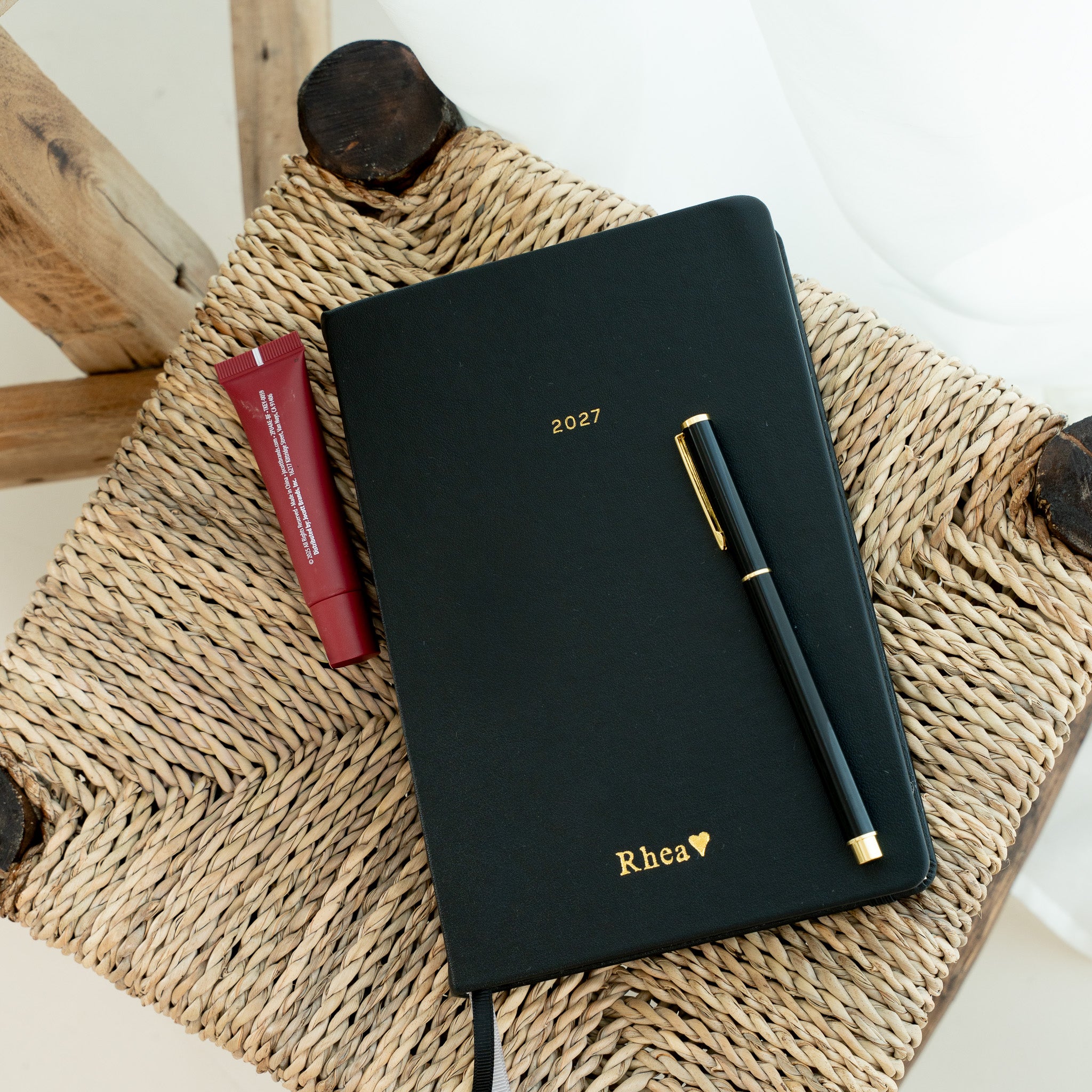 A black 2027 planner with gold foil lettering and a black pen 
